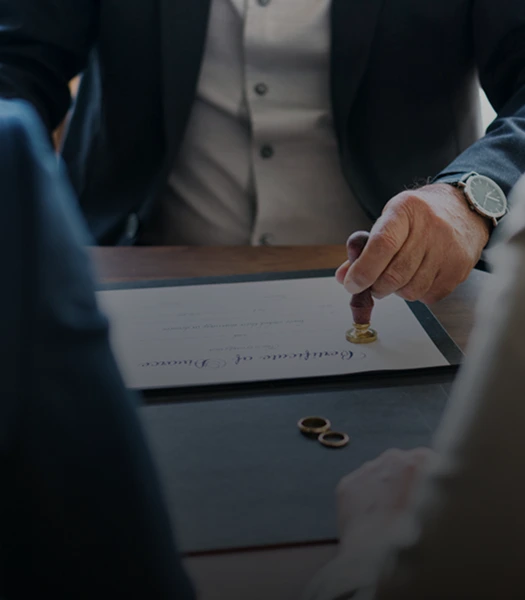 A person stamping a divorce certificate on a desk, with wedding rings placed nearby, indicating the finalization of a cooperative divorce.