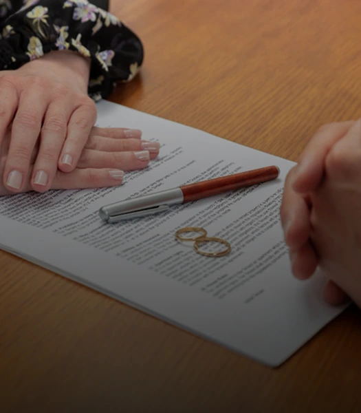 Two people sitting at a table with a legal document, a pen, and two wedding rings, symbolizing a prenuptial agreement discussion.