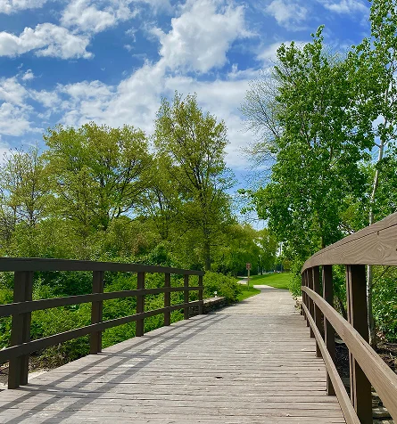 A wooden bridge extends towards a lush green park, inviting visitors to explore the natural surroundings.