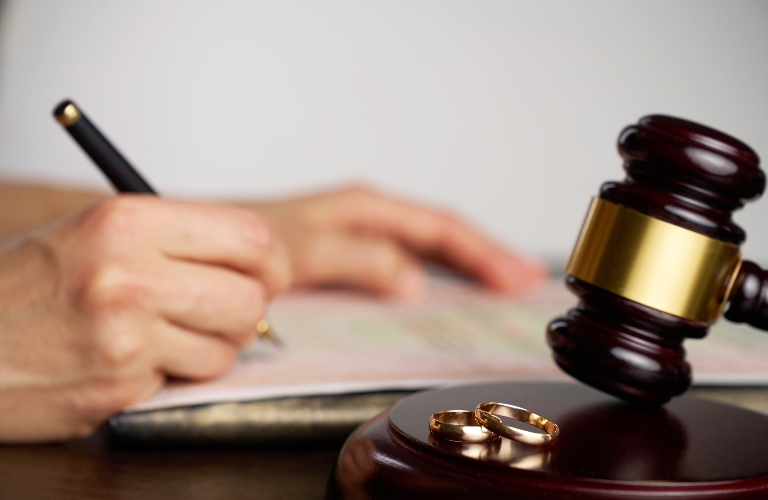 person signing divorce document, with a judge gavel and wedding rings in focus