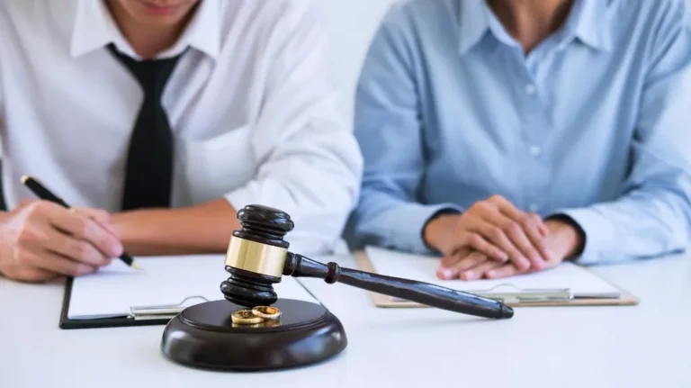 Two individuals in formal attire seated at a table with a judge's gavel and wedding rings.