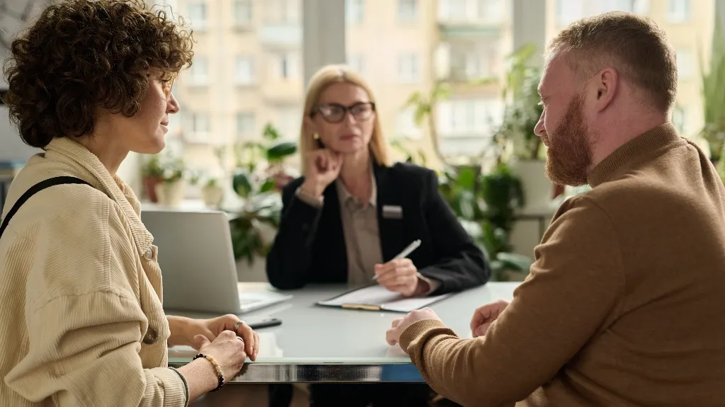 Three professionals engaged in a discussion around a table in a bright office.