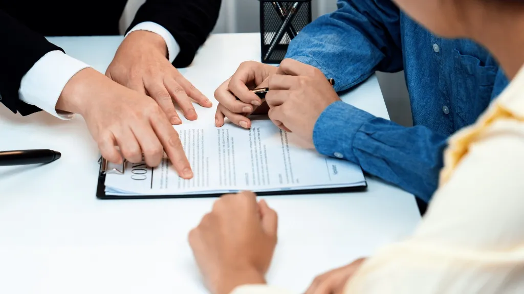 Three individuals reviewing and pointing at a contract document on a white table.