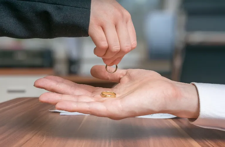 Two hands exchanging gold wedding rings over a wooden table in a formal setting.