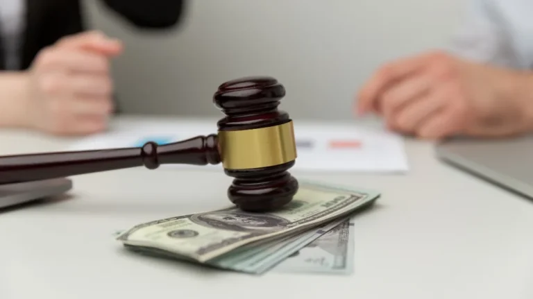 Wooden judge gavel resting on a stack of US dollar bills on a white table.