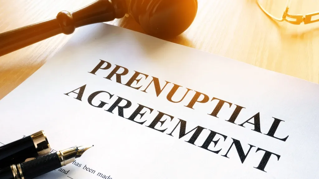 Close-up of a prenuptial agreement document with a wooden gavel and fountain pen on a light wooden surface.
