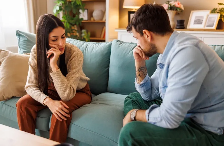 Two individuals seated on a teal sofa in a living room, appearing thoughtful and engaged in conversation.
