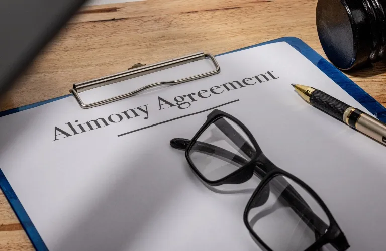 Close-up of an alimony agreement document on a blue clipboard with black eyeglasses and a pen.