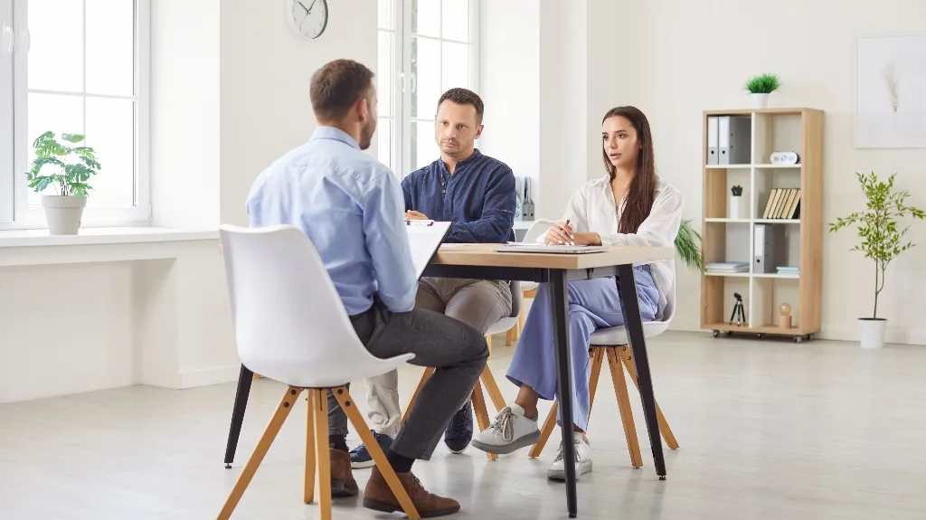 Three professionally dressed individuals seated around a table in a bright, modern office during a discussion.