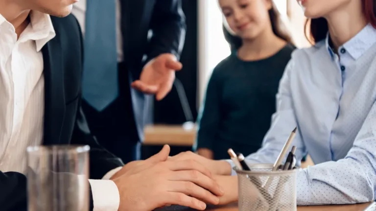 Two adults holding hands across a table with a child standing in the background.