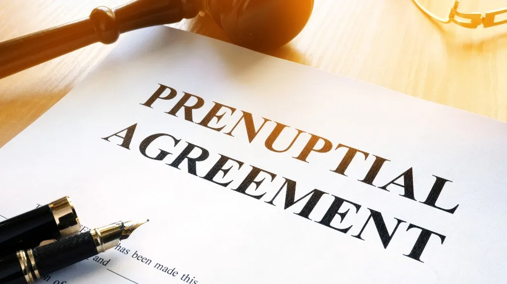 Close-up of a prenuptial agreement document with a fountain pen and wooden gavel on a wooden surface.