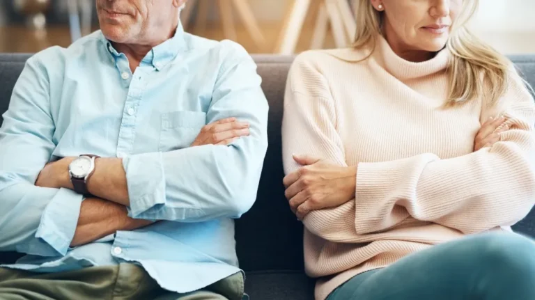 Middle-aged man and woman sitting on sofa with arms crossed, facing away from each other.