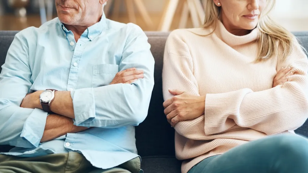 Middle-aged man and woman sitting on sofa with arms crossed, facing away from each other.