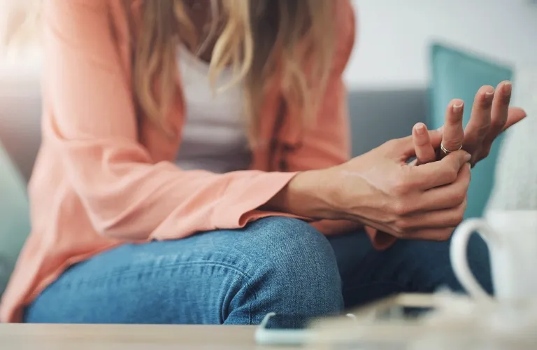 Woman in casual attire sitting on couch, holding and examining her wrist.