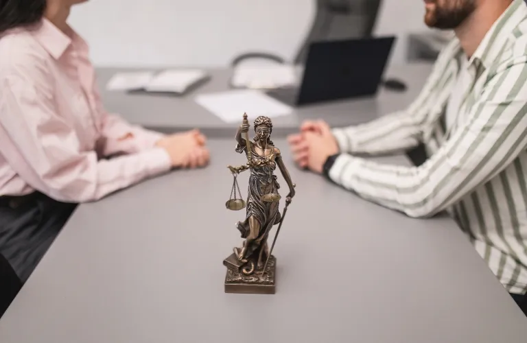 Bronze Lady Justice statue on gray table between two people in business attire.