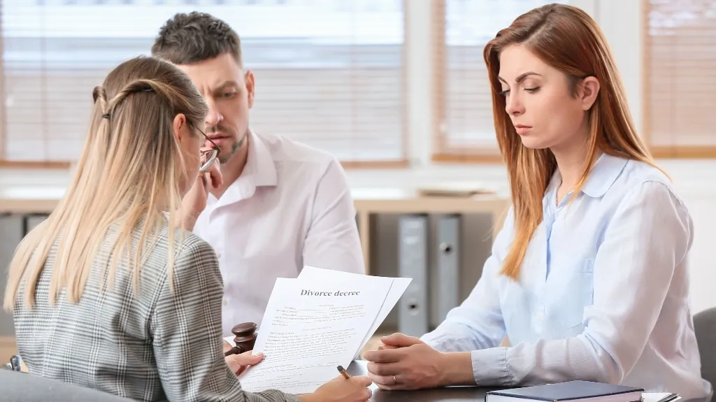 Three adults in a formal office setting reviewing a divorce decree document.