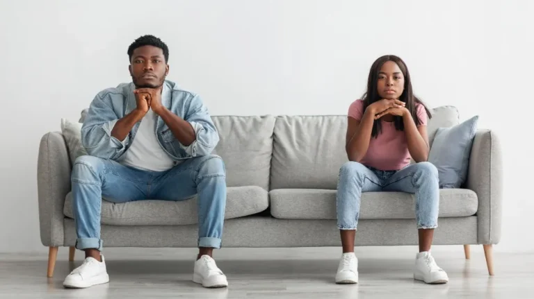 Two young adults sitting apart on a gray couch, looking serious and contemplative.