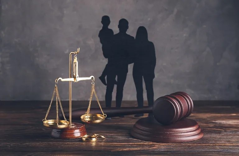 Golden scales of justice and wooden gavel with family shadow on textured gray background.