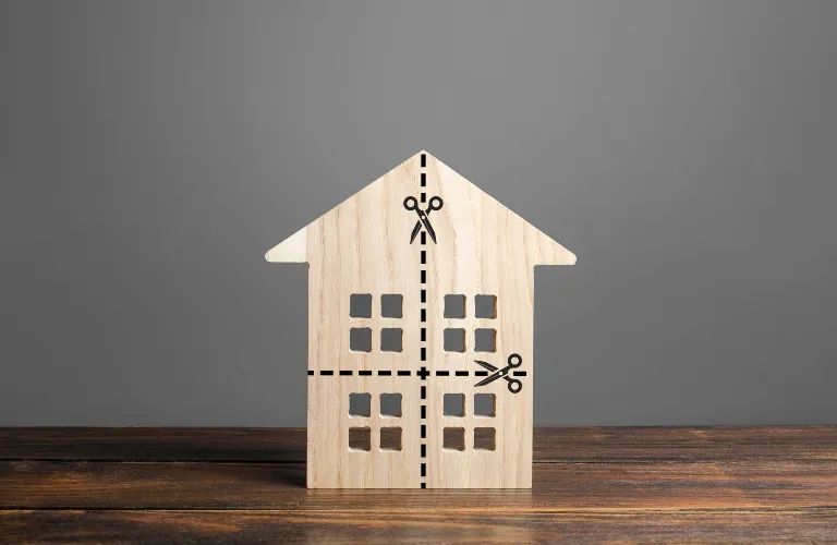 Wooden house model with black dashed cut lines and scissor icons on wooden surface.