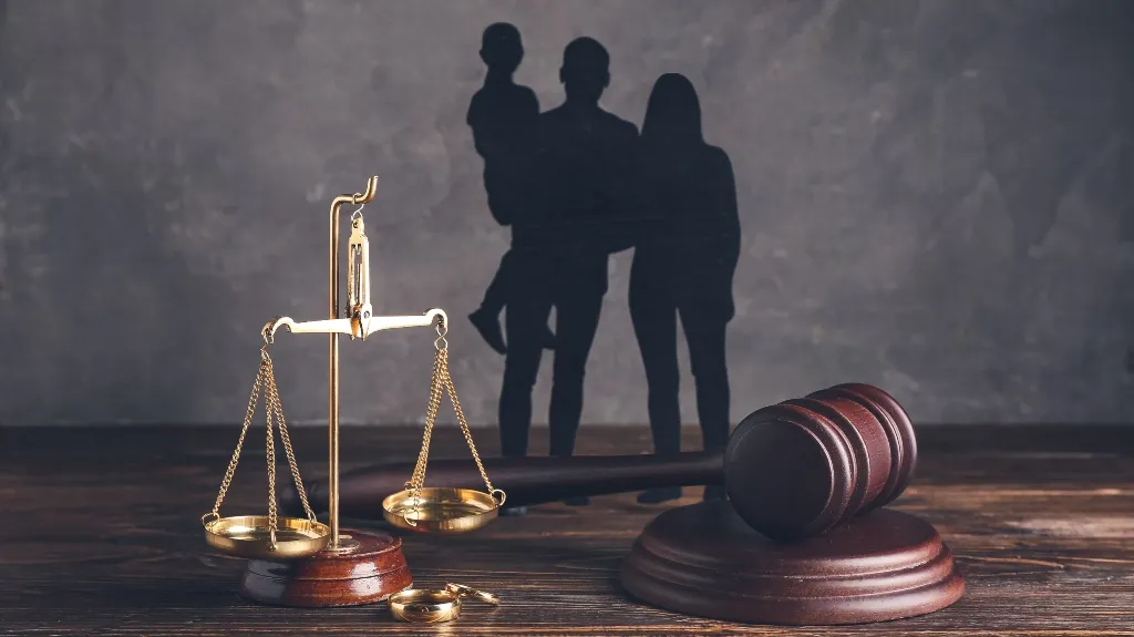 Golden balance scales and wooden judge gavel on table with family silhouettes background.