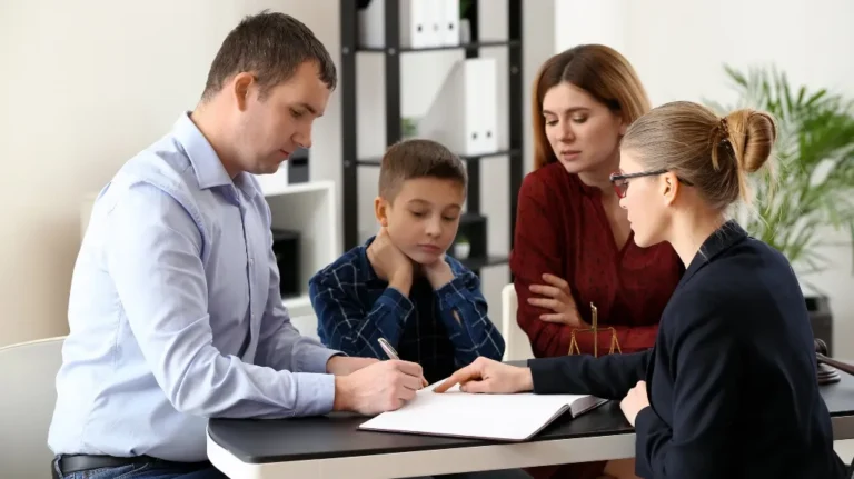 Professional woman explaining documents to a man, woman, and child at office desk.