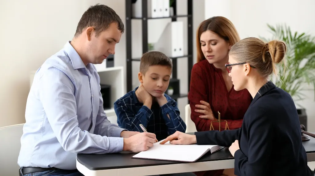 Professional woman explaining documents to a man, woman, and child at office desk.