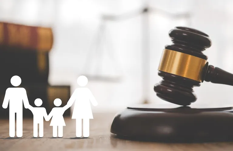 Wooden judge's gavel with family icons and blurred legal books and scales in background.