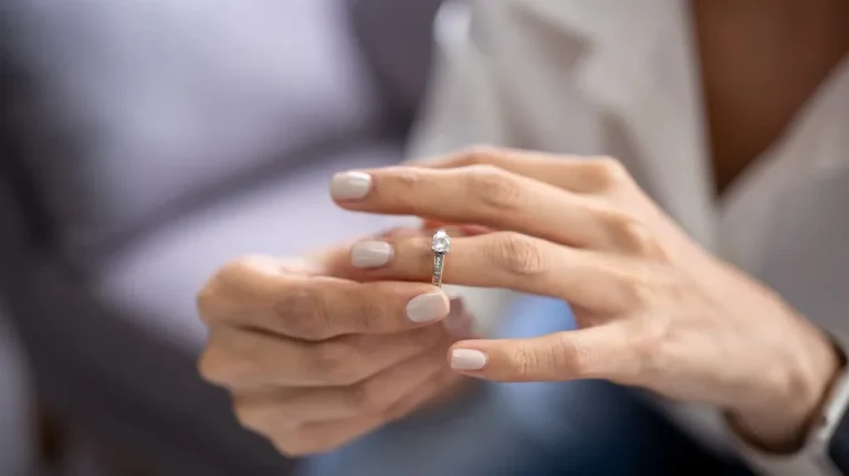 Close-up of hands with light-colored nail polish holding a diamond engagement ring.